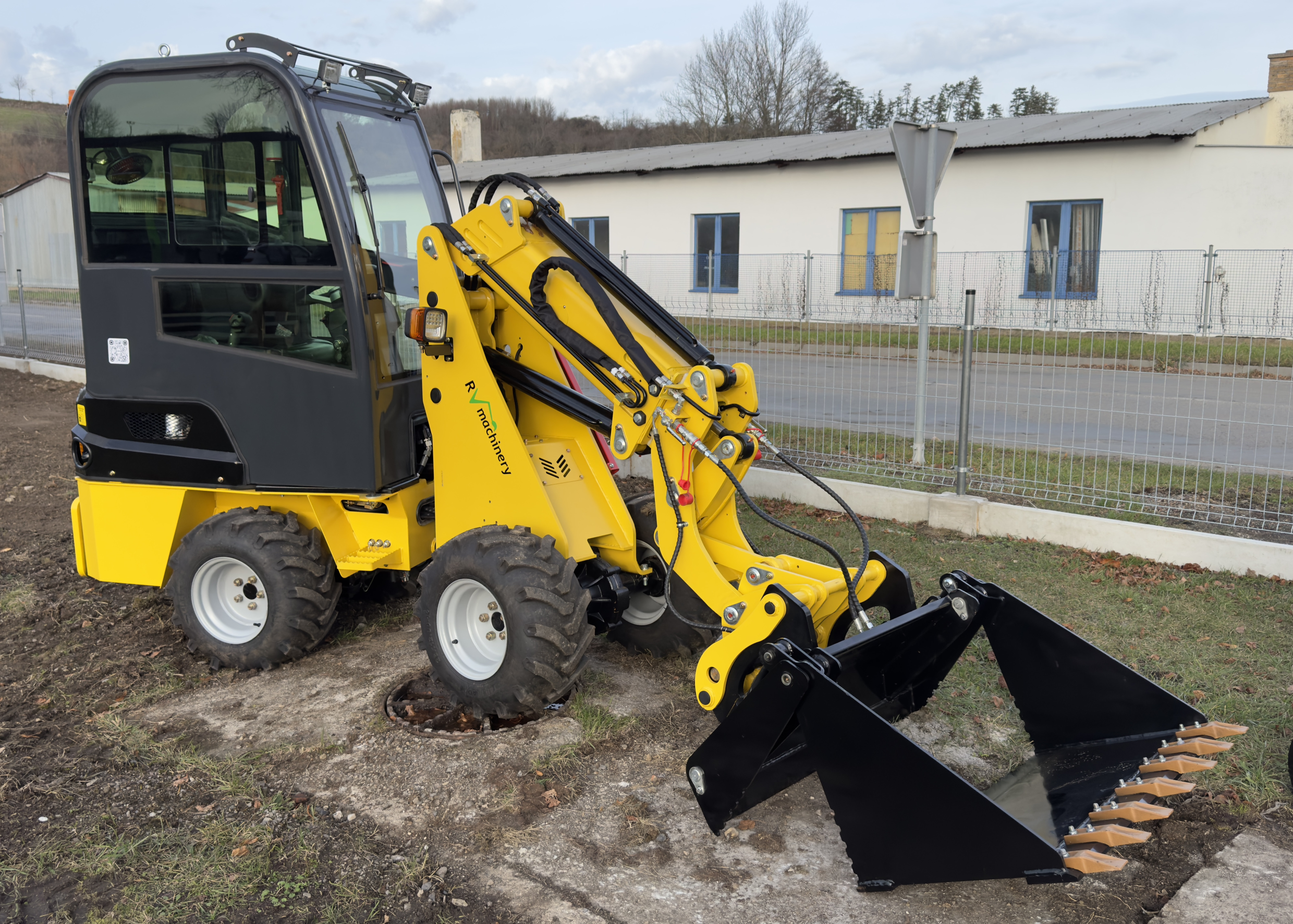 Pravý boční pohled na kloubový teleskopický mininakladač R906TS, zobrazující jeho robustní rám a schopnost manipulovat těžkým materiálem.